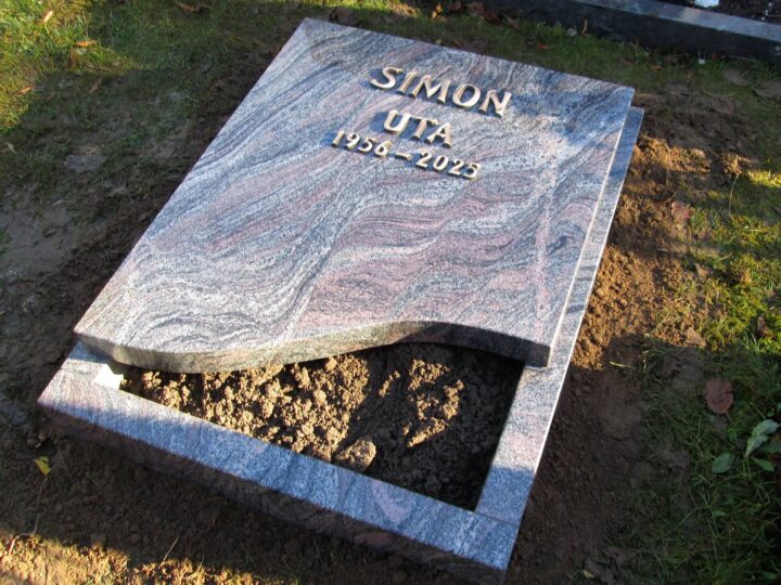 Grabmal Nr. 42: Grababdeckplatte aus rötlich gemasertem Granit mit geschwungener Kante und Bronzeschrift auf einer Einfassung