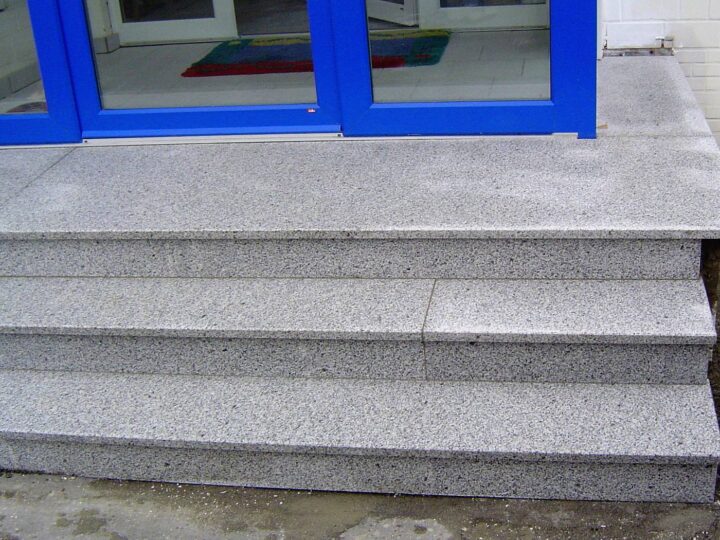 Drei Eingangsstufen mit Podest aus hellgrauem Granit vor einer Glastür
